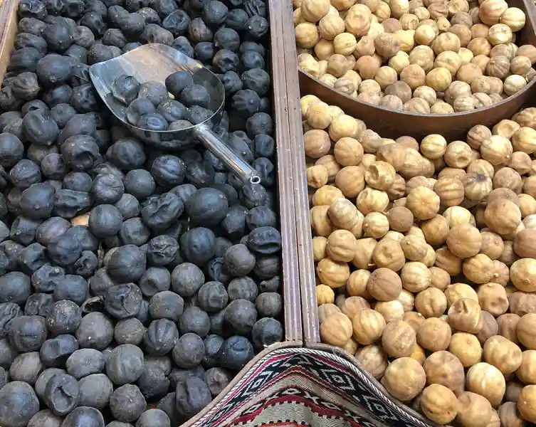 فله‌ای از لیمو عمانی سیاه و لیمو عمانی زرد، جدا شده توسط یک جداکننده چوبی با یک قاشق فلزی روی لیمو عمانی سیاه.